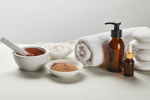 Sea salt and clay in bowls, cotton towel, stones, bottles on white table isolated on grey — Stock Photo