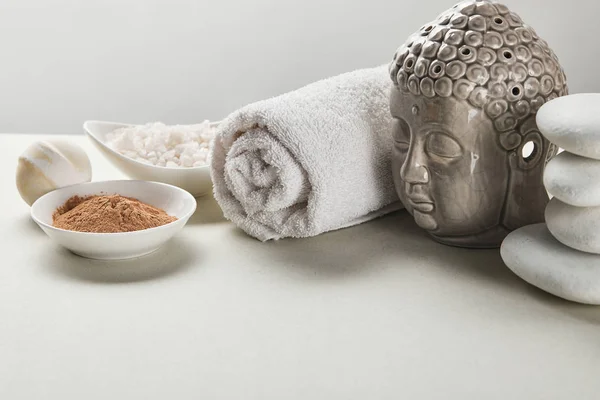 Морская соль и глиняный порошок в мисках, хлопковое полотенце, камни, бомба для ванны и статуэтка Будды на белом столе, изолированном на сером — стоковое фото