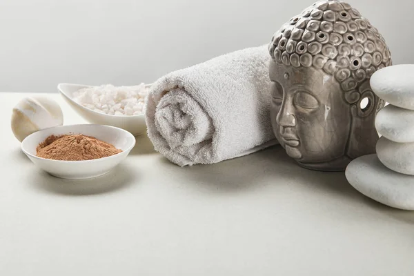 Sel de mer et poudre d'argile dans des bols, serviette de coton, pierres, bombe de bain et figurine de Bouddha sur table blanche isolée sur gris — Photo de stock