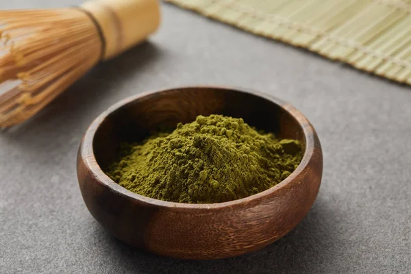 Selective focus of bamboo whisk and green matcha powder in wooden bowl on grey table with copy space — Stock Photo