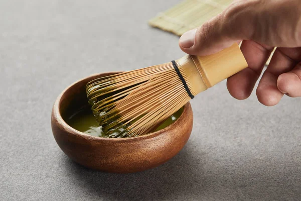 Selective focus of man holding bamboo whisk in wooden bowl with green matcha — Stock Photo
