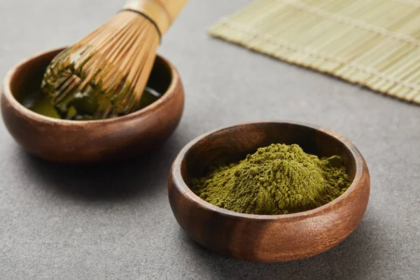 Selective focus of green matcha powder and bamboo whisk in wooden bowl with tea — Stock Photo