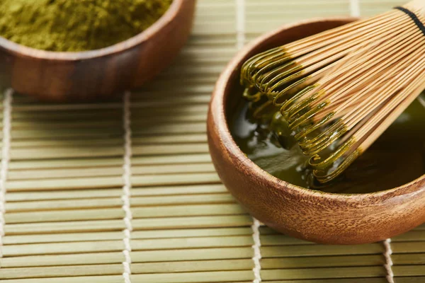 Foco selectivo de polvo de matcha verde y batidor de bambú en tazón de madera con té - foto de stock