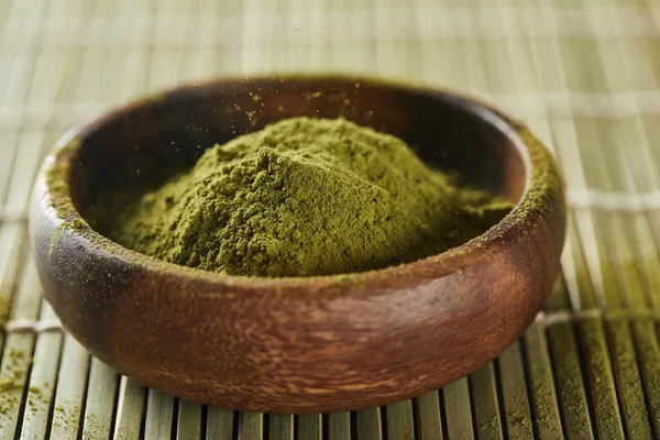 Selective focus of green matcha powder in wooden bowl on bamboo table mat — Stock Photo