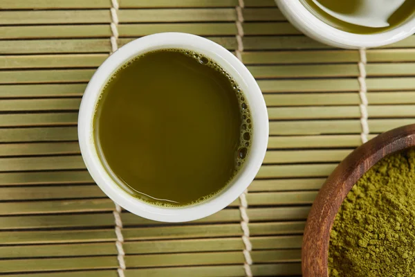 Vue du dessus des tasses blanches avec thé vert près de poudre de matcha dans un bol en bois — Photo de stock