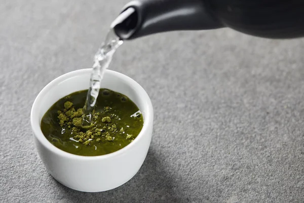Schwarzer Wasserkocher gießt Wasser in weiße Tasse mit grünem Matcha-Pulver — Stockfoto
