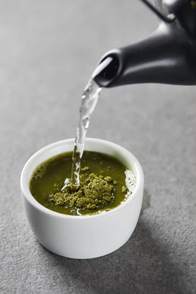 Black kettle pouring water in white cup with green matcha powder — Stock Photo