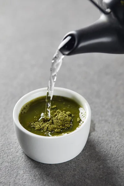 Schwarzer Wasserkocher gießt Wasser in weiße Tasse mit grünem Matcha-Pulver — Stockfoto