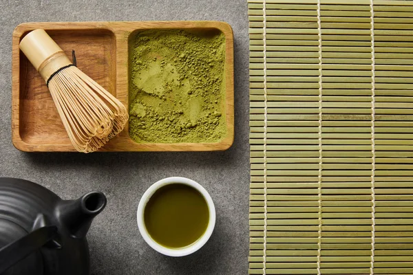 Ansicht von Bambusbesen mit Matcha-Pulver in Holzschüssel in der Nähe von weißer Tasse, schwarzer Teekanne und Untersetzer — Stockfoto