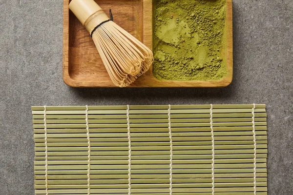Top view of bamboo whisk and green matcha powder on board near table mat — Stock Photo