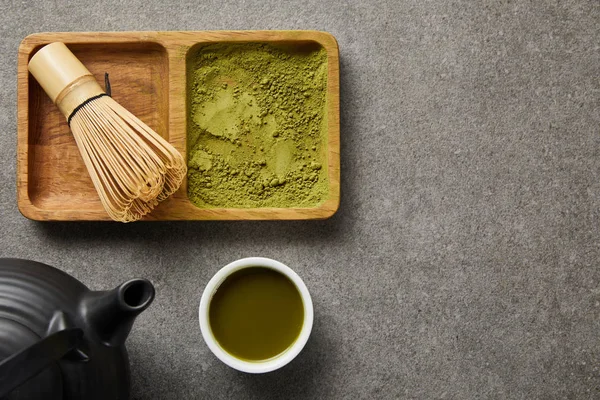 Vista superior de batedor de bambu e pó de matcha a bordo perto de bule preto e xícara branca com chá verde — Fotografia de Stock