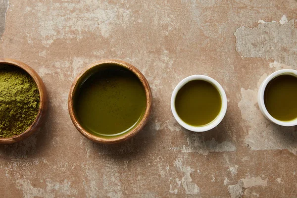 Top view of matcha powder, bowl and cups with green tea on aged surface — Stock Photo