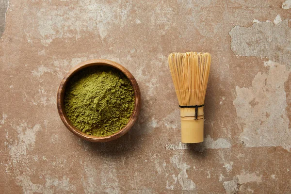 Top view of matcha powder in wooden bowl with bamboo whisk on aged surface — Stock Photo