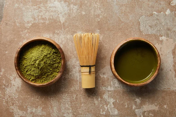 Vista dall'alto di tè matcha e polvere in ciotola di legno con frusta di bambù su superficie invecchiata — Foto stock