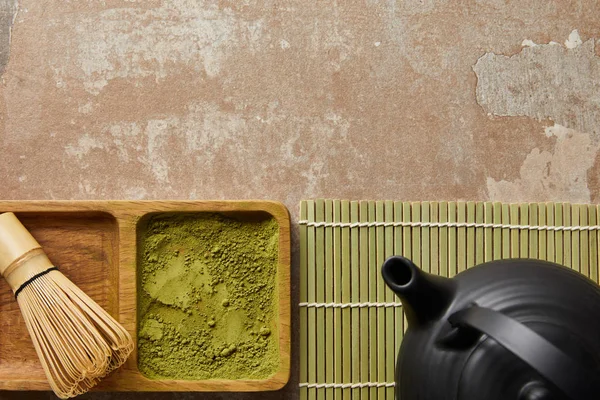 Vista dall'alto di polvere di matcha e frusta di bambù a bordo vicino alla teiera nera sulla superficie invecchiata — Foto stock