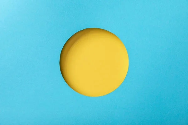 Blue paper background with minimalistic yellow round hole — Stock Photo