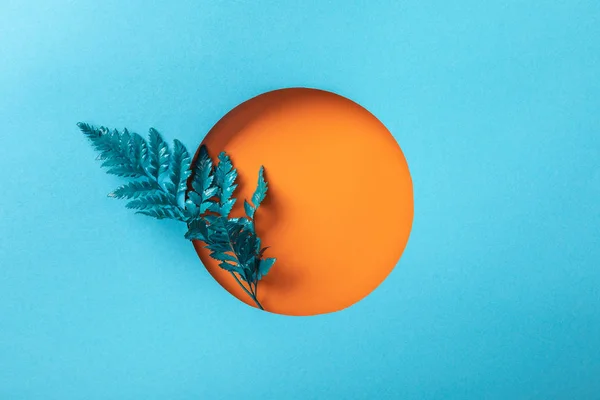 Hoja decorativa azul en agujero redondo naranja sobre papel azul - foto de stock