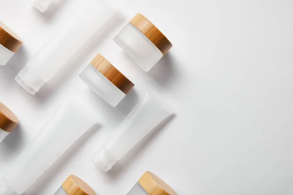 Disposición plana de tubos de crema y frascos con tapas de madera en blanco - foto de stock