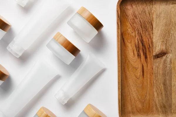 Flat lay of cream tubes and jars near wooden tray on white — Stock Photo