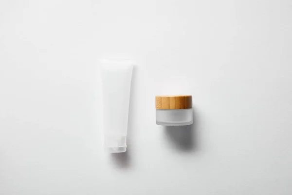 Vista superior del frasco con tapa de madera y tubo de crema en blanco - foto de stock