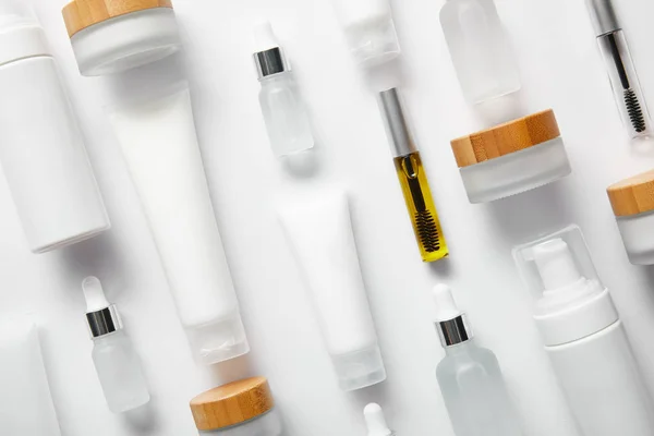 Disposición plana de tubos de crema con crema de manos, botellas de rímel, botellas de vidrio cosmético, dispensadores de cosméticos y frascos en blanco - foto de stock