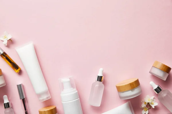 Vista superior de tubos de crema, dispensador de cosméticos, frascos vacíos y con crema de manos, botellas de rímel en rosa - foto de stock