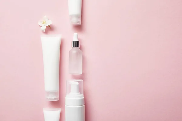 Pose plate de bouteille en verre cosmétique, tubes à crème avec crème, distributeur de cosmétiques et fleur de jasmin sur rose — Photo de stock