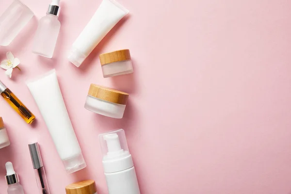 Top view of different cosmetic containers and jasmine flower on pink — Stock Photo