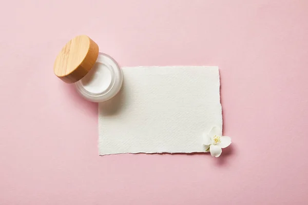 Vista dall'alto di vaso con crema, pezzo di carta e fiore di gelsomino su rosa — Foto stock