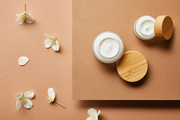 Top view of open jars with cream and scattered jasmine flowers on brown — Stock Photo