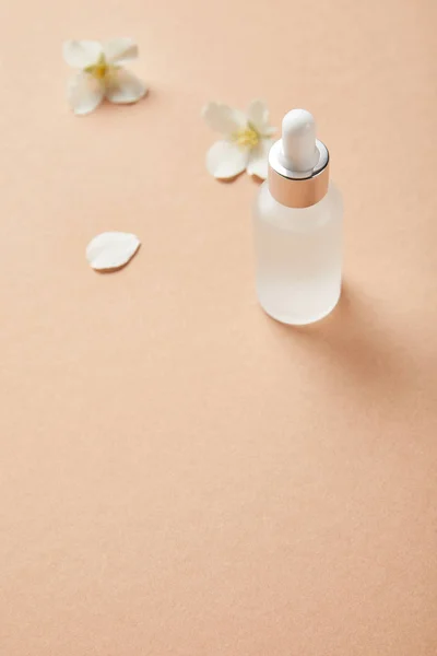 Cosmetic glass bottle near jasmine flowers on beige — Stock Photo