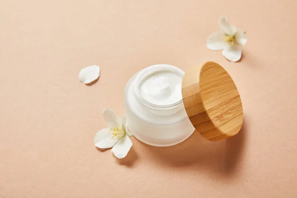 Open jar with cream and few jasmine flowers on brown — Stock Photo