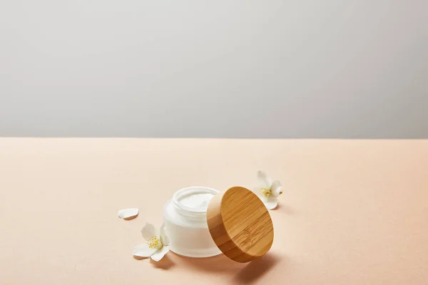 Pot ouvert avec crème pour le visage et peu de fleurs de jasmin sur beige isolé sur gris — Photo de stock
