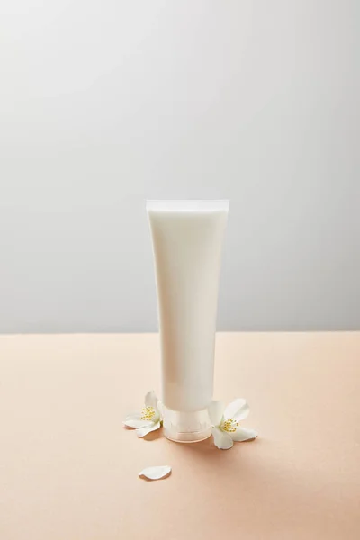 Tubo de creme com creme de mão e poucas flores de jasmim no bege — Fotografia de Stock