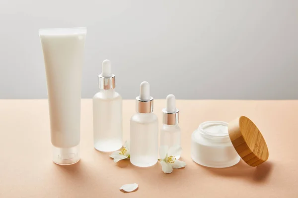 Tubo crema, bottiglie di vetro cosmetico con siero e vaso aperto con crema vicino a pochi fiori di gelsomino — Foto stock