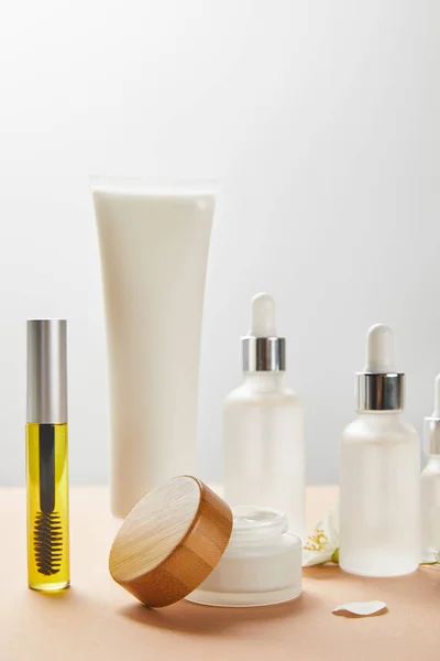 Bouteille de mascara avec huile naturelle, tube à crème, bouteilles en verre cosmétique, pot ouvert avec capuchon en bois et fleur de jasmin sur beige — Photo de stock