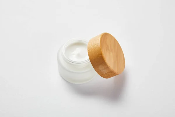 Frasco de vidrio abierto con crema y tapa de madera en blanco - foto de stock