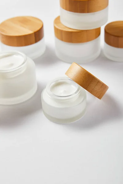 Bocaux en verre avec crème et bouchons en bois sur blanc — Photo de stock