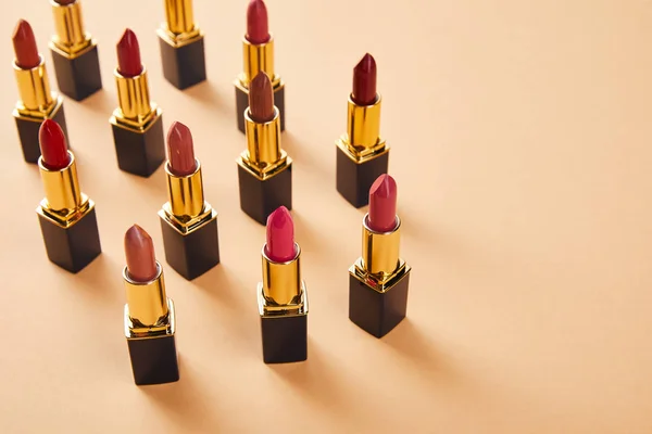 Diferentes tonos rojos de lápices labiales en beige con espacio de copia — Stock Photo