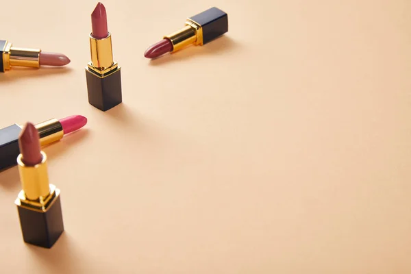 Différentes nuances de rouge à lèvres en tubes sur beige avec espace de copie — Photo de stock