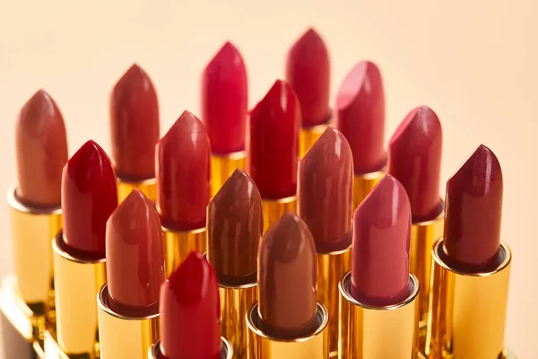 Gros plan de différentes nuances rouges de rouge à lèvres dans des tubes isolés sur beige — Photo de stock