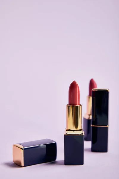 Various shiny lipsticks in tubes on violet — Stock Photo