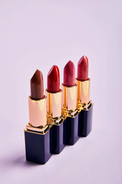 Various red lipsticks in tubes on violet — Stock Photo