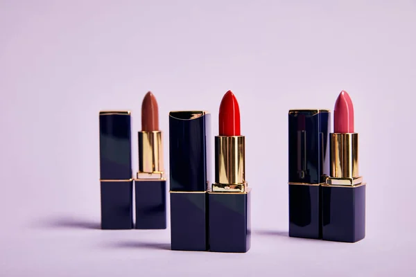 Différentes nuances rouges de rouges à lèvres en tubes sur violet — Photo de stock