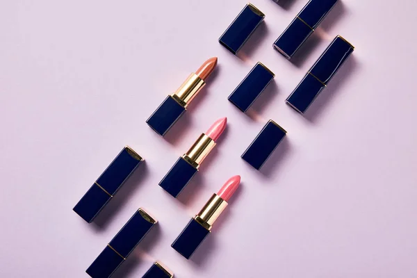 Flache Lage mit verschiedenen rosa Schattierungen von Lippenstiften in Röhren auf violett — Stockfoto