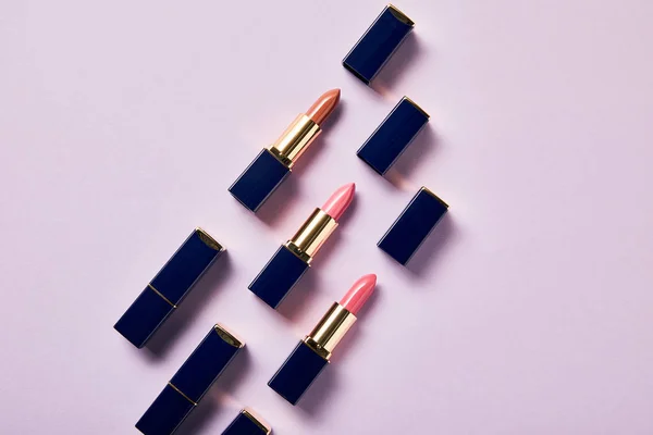 Flat lay with various pink shades of lipsticks in tubes on purple — Stock Photo