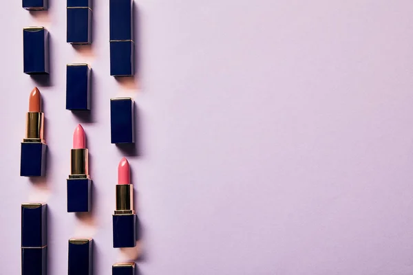 Flache Lage mit verschiedenen rosa Schattierungen von Lippenstiften auf violett mit Kopierraum — Stockfoto