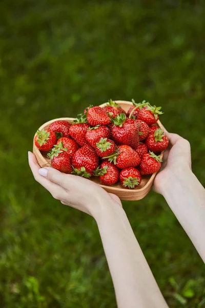 Vista recortada de la mujer sosteniendo plato en forma de corazón con fresas dulces - foto de stock