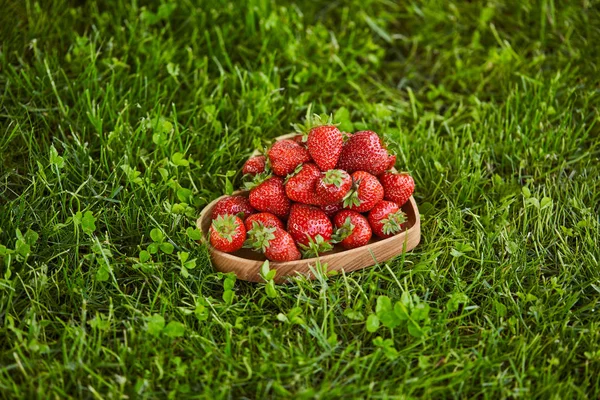 Red strawberries in wooden heart shaped plate on green grass — Stock Photo