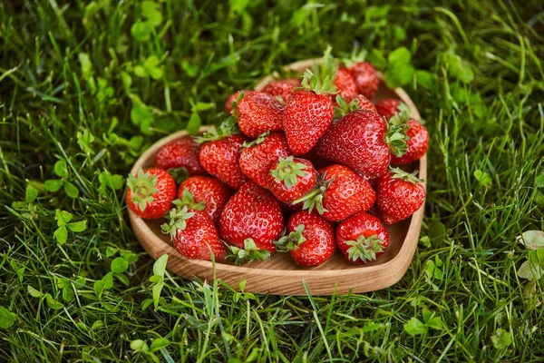 Fresas frescas en plato en forma de corazón de madera sobre hierba verde — Stock Photo